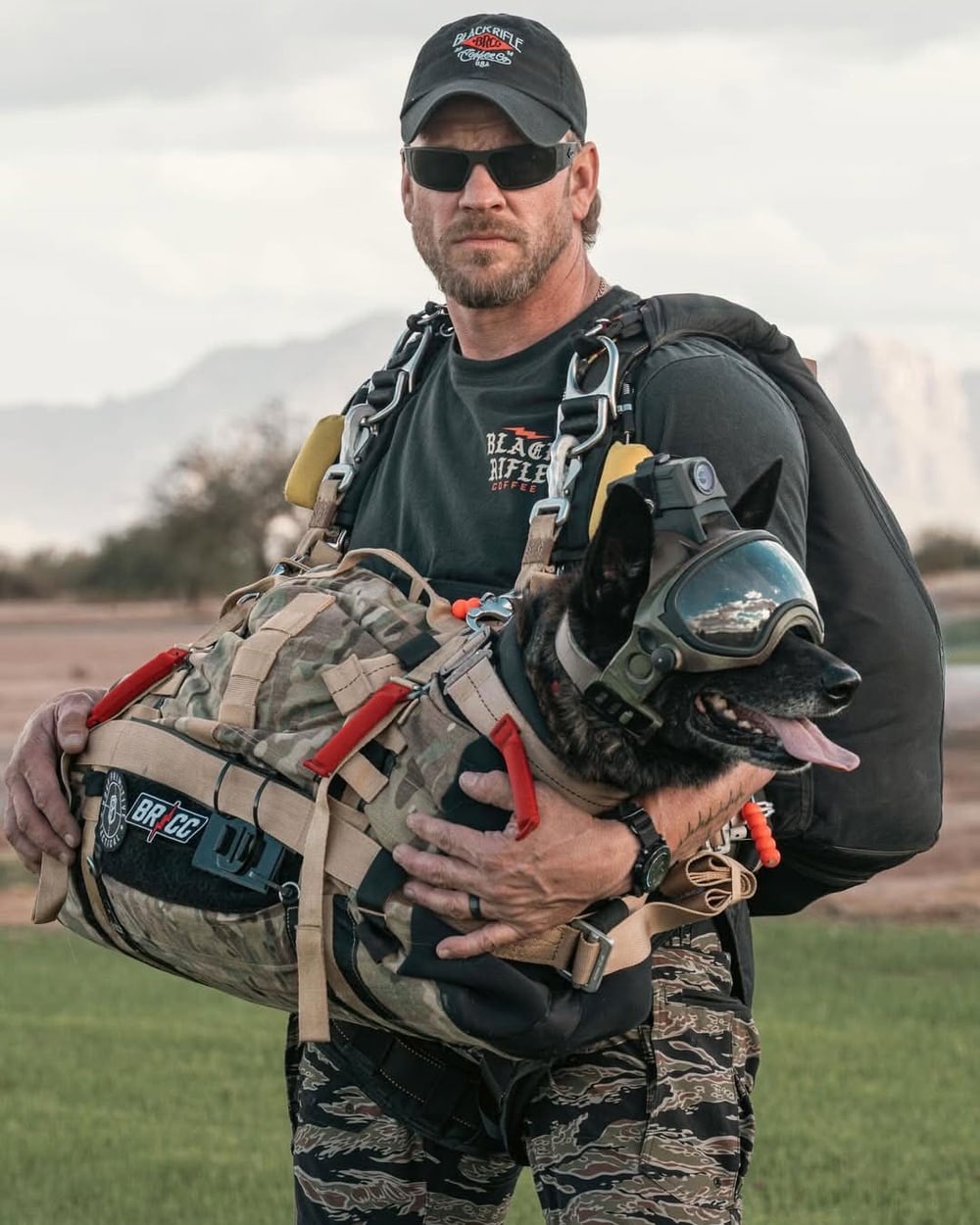 Byron Beplay holding a goggled K9 in a tactical pack, freefall rig over shoulder